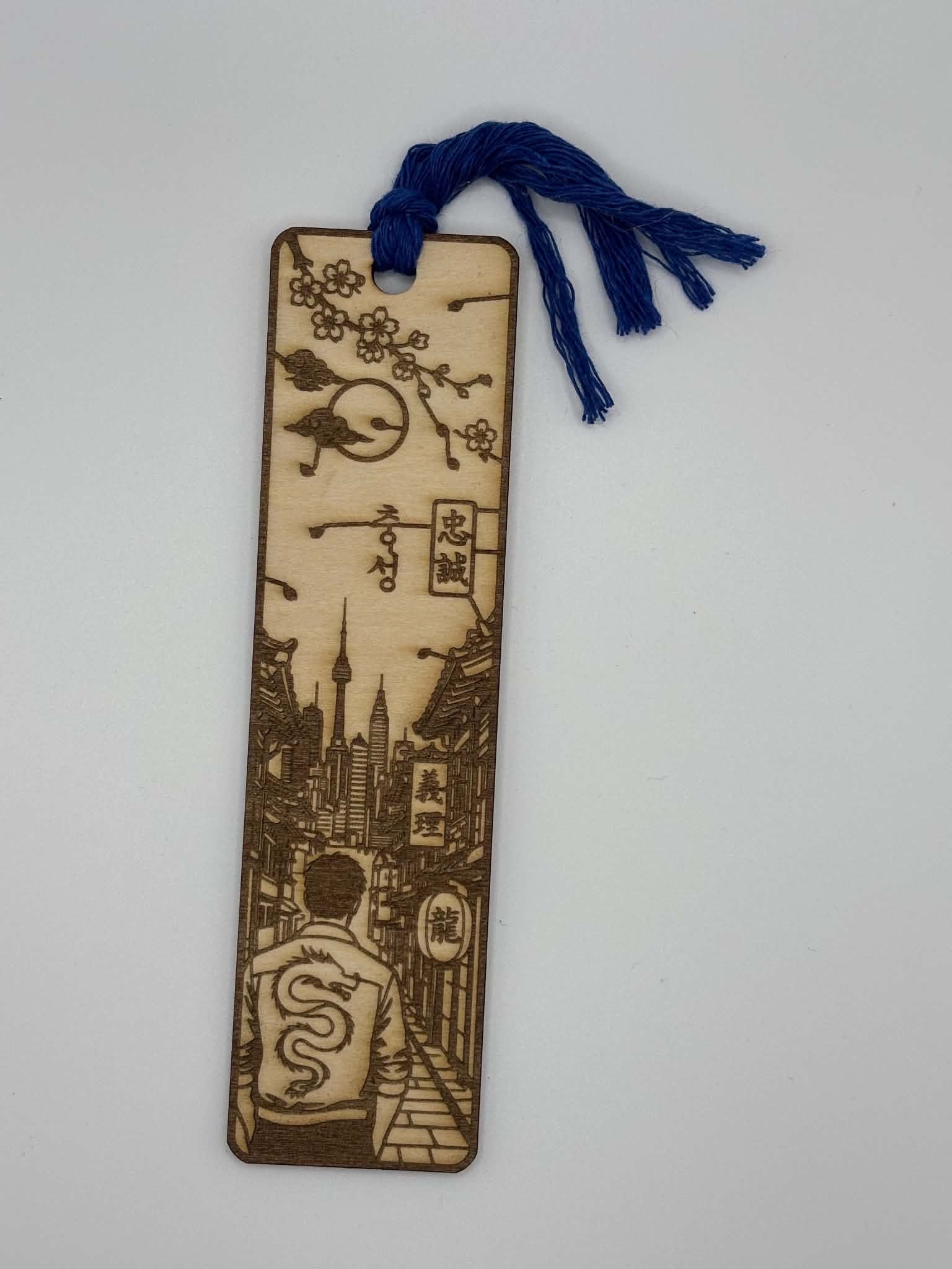 Découvrez ce marque-page en bois gravé au laser inspiré du Japon. Paysage japonais, fleurs de cerisier, dragon et pompon bleu. Fabrication artisanale française.