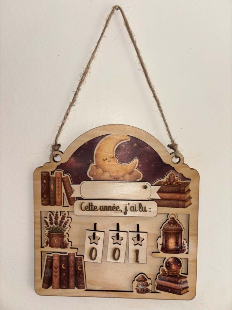Compteur de lecture en bois personnalisable représentant une lune endormie entourée de livres, d'une lanterne et d'éléments inspirés des univers fantastiques. Les chiffres amovibles permettent de suivre facilement les lectures réalisées au cours de l'année.