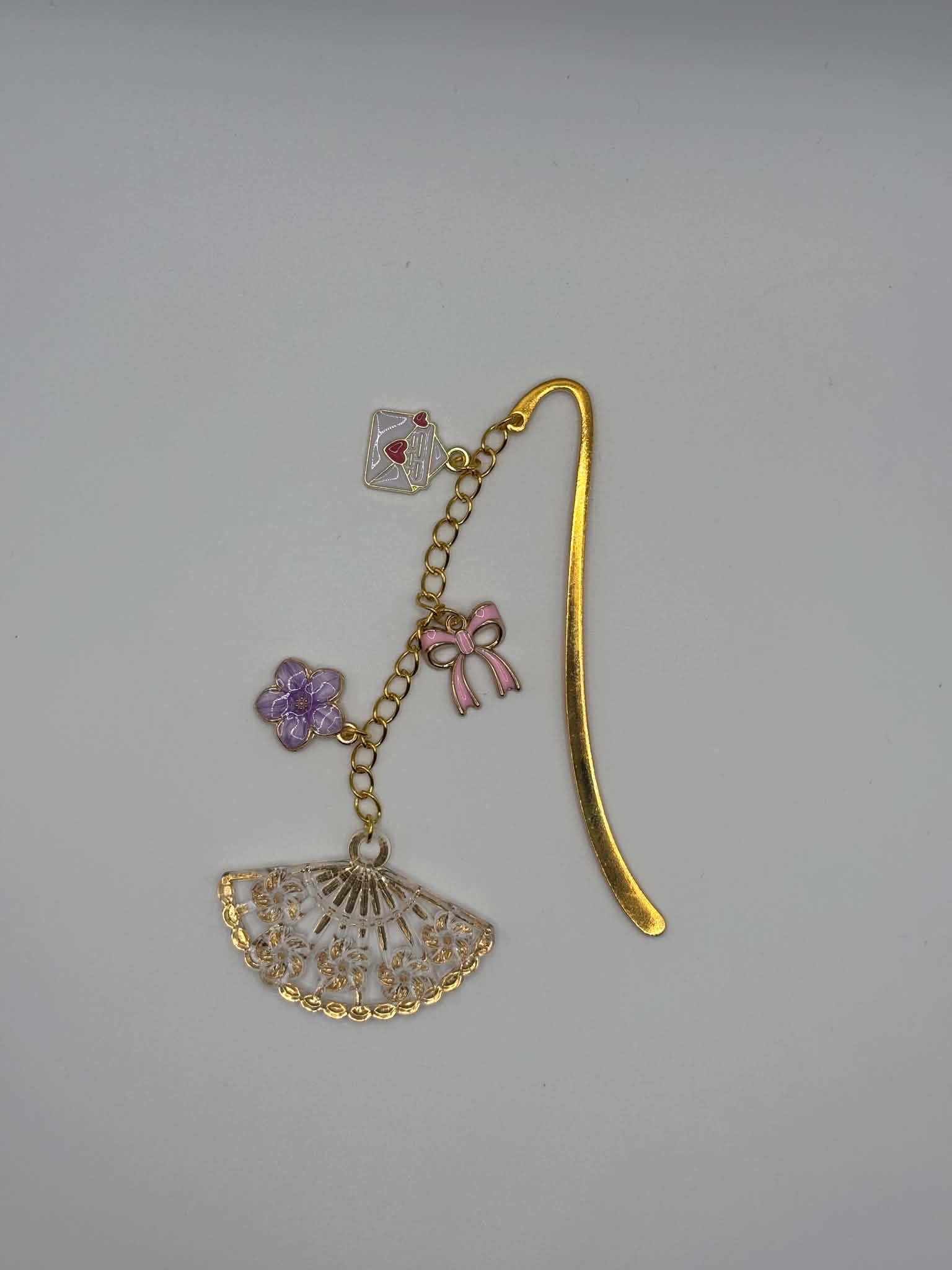 Marque-page en métal doré décoré d'un éventail ajouré, d'une fleur violette, d'un nœud rose et d'une enveloppe suspendue, idéal pour les passionnés de lecture.