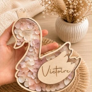 Carte étape bébé en bois en forme de cygne personnalisée avec prénom, décorée de fleurs séchées et équipée d'ailes interchangeables indiquant les mois de bébé.