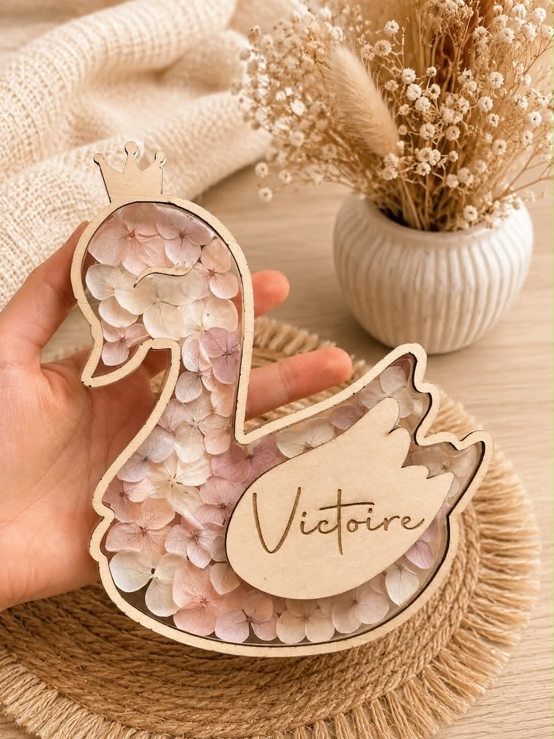Carte étape bébé en bois en forme de cygne personnalisée avec prénom, décorée de fleurs séchées et équipée d'ailes interchangeables indiquant les mois de bébé.
